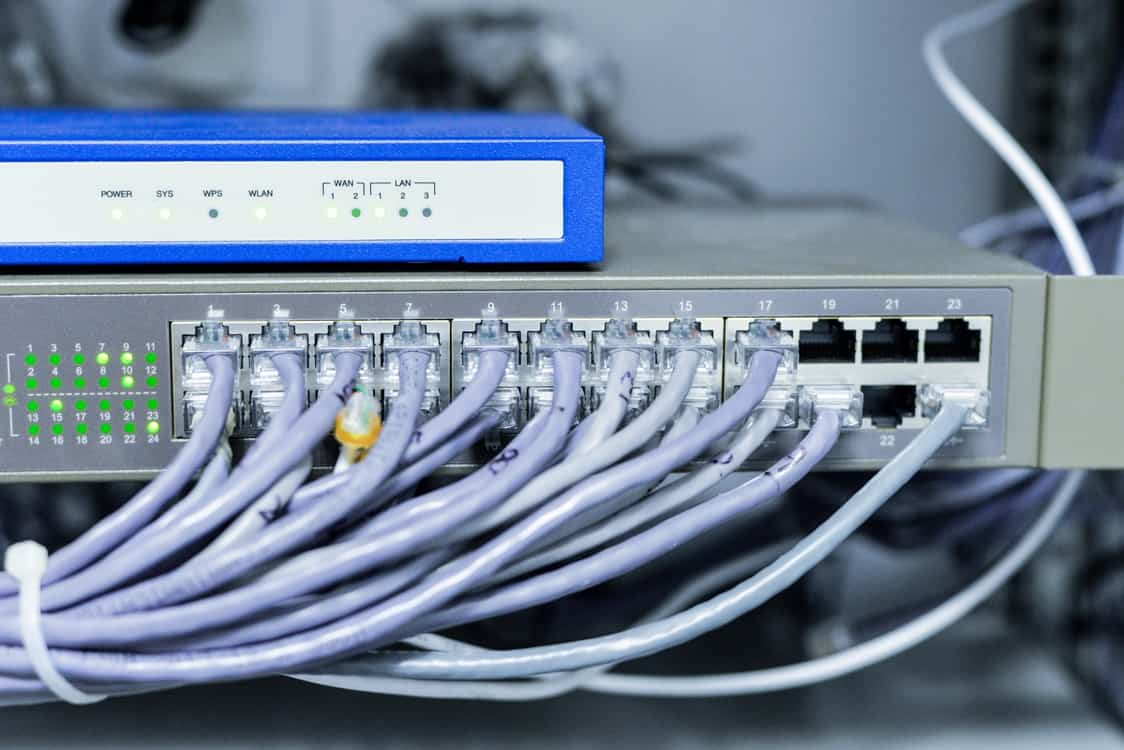 Network switch with Ethernet cables connected. The front panel shows indicator lights and numbered ports, with a blue network router above it.
